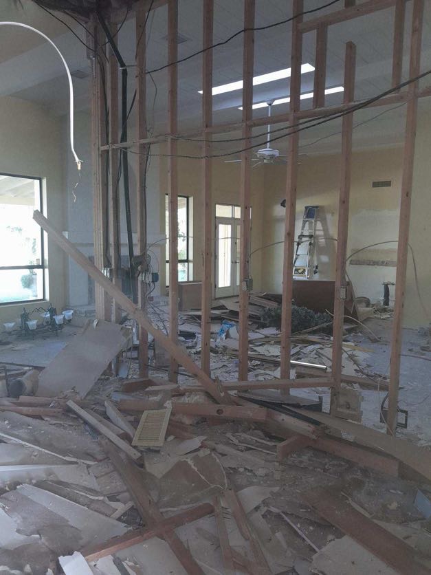 Residential area with a home mid-demolition, dust rising as walls crumble.